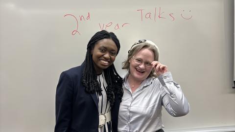 Kristen and Genia hug and smile in front of a whiteboard